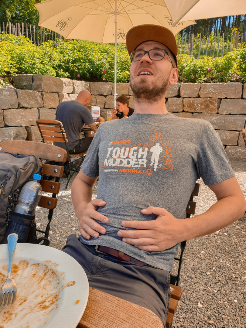 Mann, der sich den Bauch hält weil er in der Gaststätte zu viel gegessen hat.