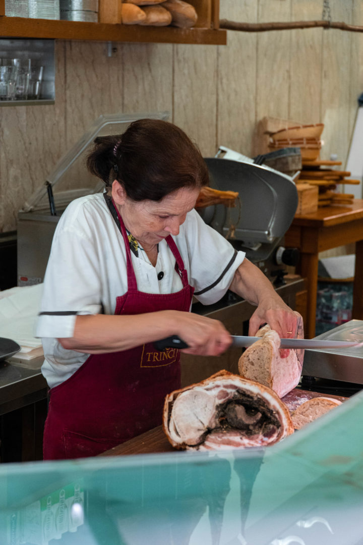 Frau schneidet die umbrische Spezialität Porchetta in Scheiben. Porchetta ist eine Art mit Kräutern gefüllter Schweinebraten.
