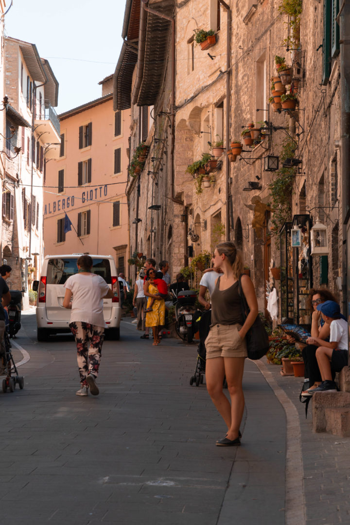 Italienische Altstadt von Assisi mit Mofafahrer und Touristen.