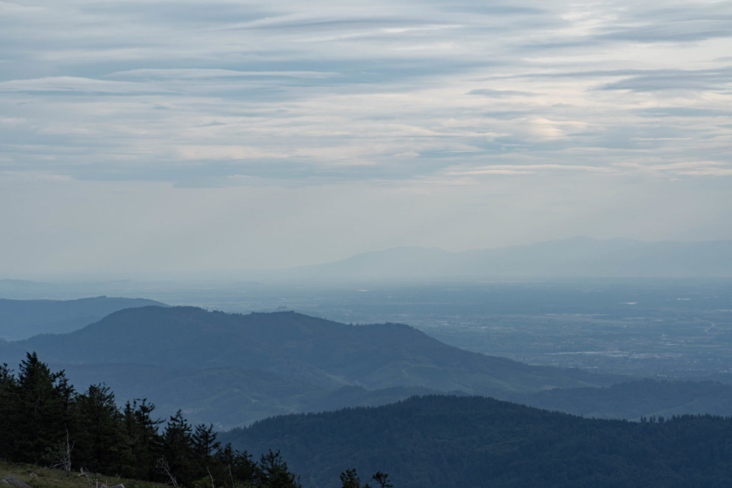 Blick über die Ausläufer des Schwarzwaldes von der Hornisgrinde aus. Der Himmel ist bewölkt, über den Bergen hängt Nebel, ein paar einzelne Sonnenstrahlen kommen durch.
